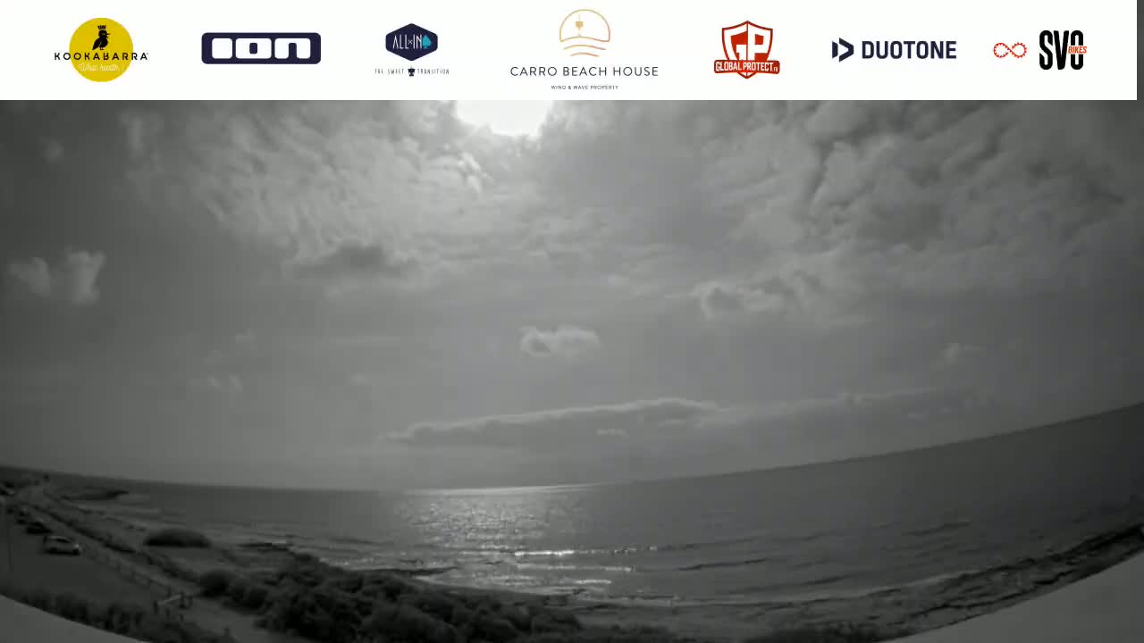 A mostly cloudy day with a calm ocean meeting a sandy shore.