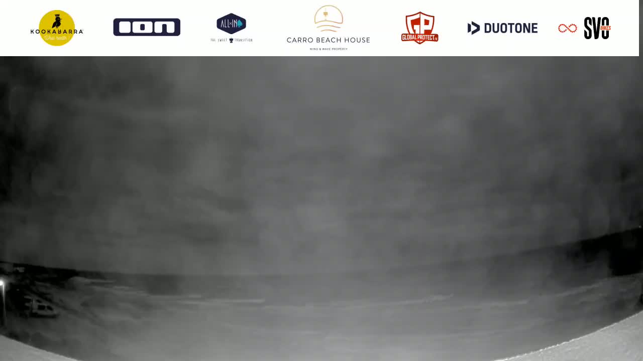 A low-light, blurry image shows a dark, possibly stormy, night scene at the coast, with a hazy or foggy atmosphere obscuring the view of the water and land.