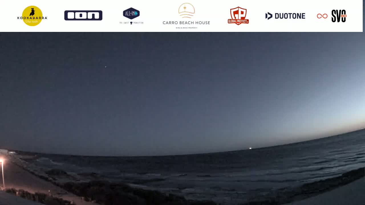 A wide shot of a dark ocean under a twilight sky shows a shoreline with a path and a single light post.