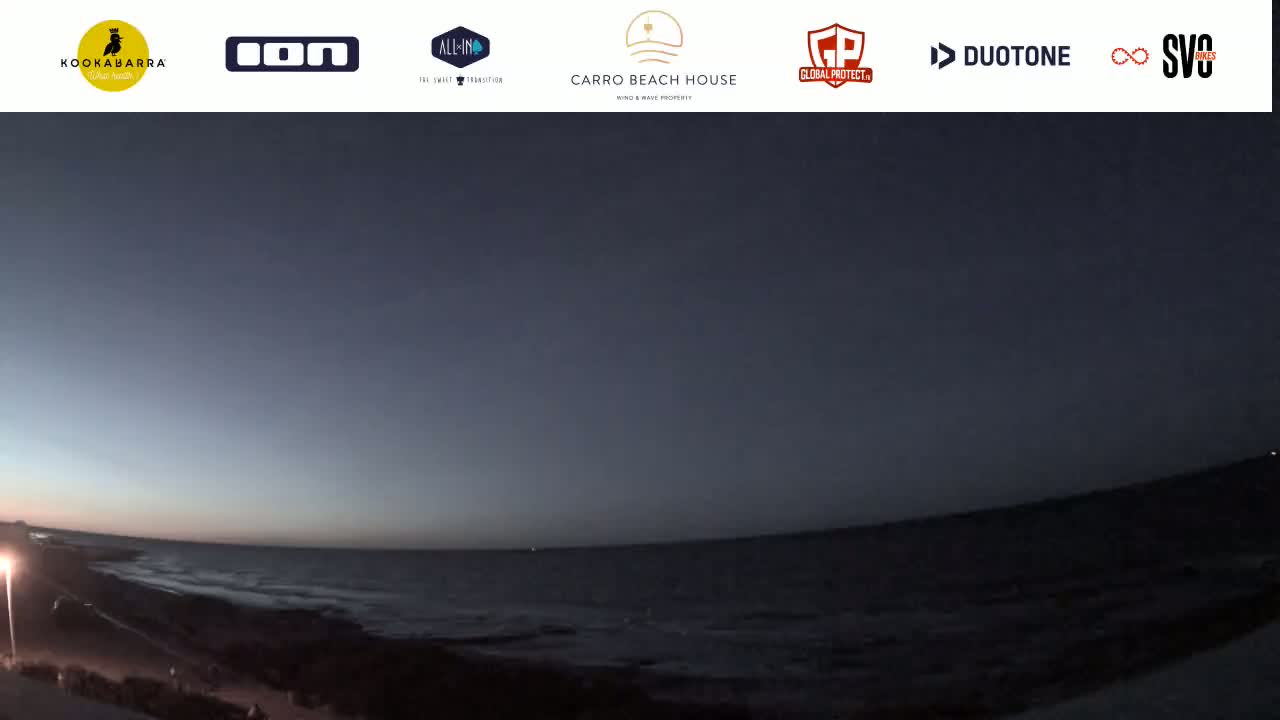 A wide shot shows a dark ocean at twilight, with a sandy shore and a few lights visible along the coast.