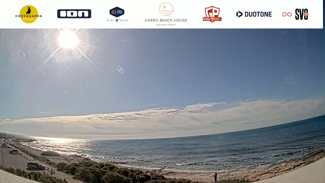 A sunny day with scattered clouds shows a wide, sandy beach next to a calm ocean.