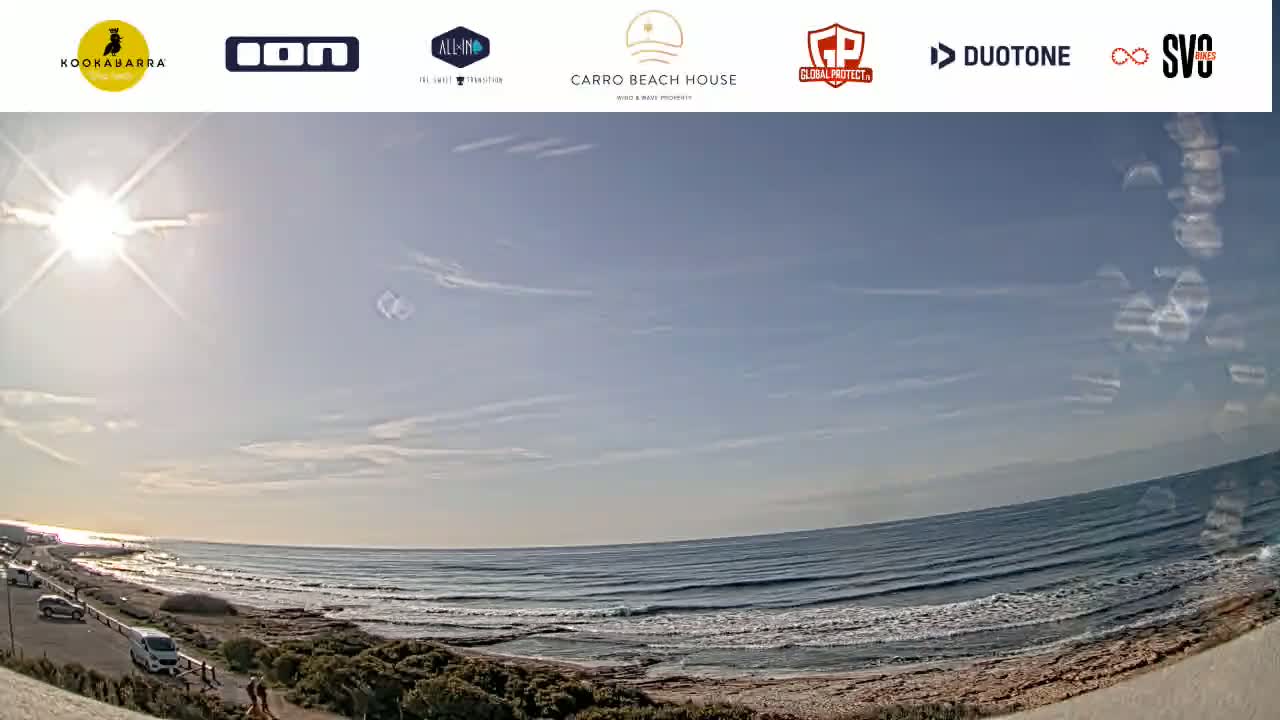 A sunny day at a beach with a mostly clear sky and moderate waves rolling onto a sandy shore.