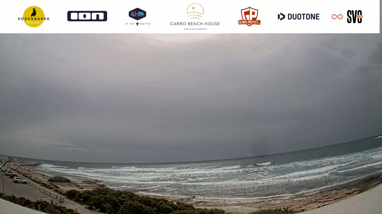 A wide, overcast view shows a sandy beach with small waves rolling into shore under a gray sky.