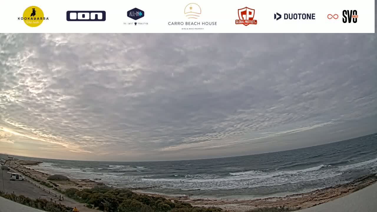 A wide, overcast sky over a rocky shoreline with a calm ocean and small waves.