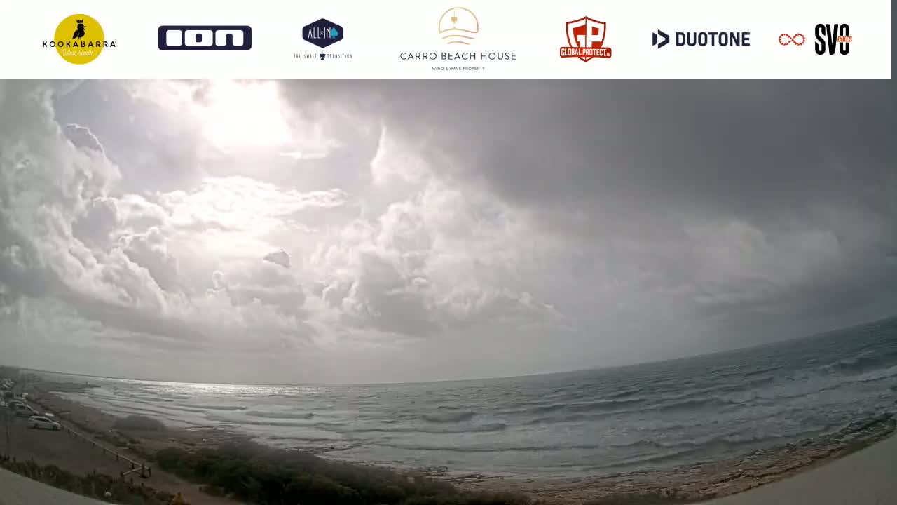 A wide shot of a beach with a partly cloudy sky and a somewhat choppy ocean.