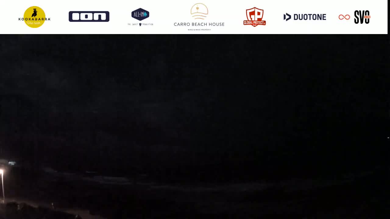 A dark nighttime coastal scene shows a mostly obscured ocean under a cloudy sky.
