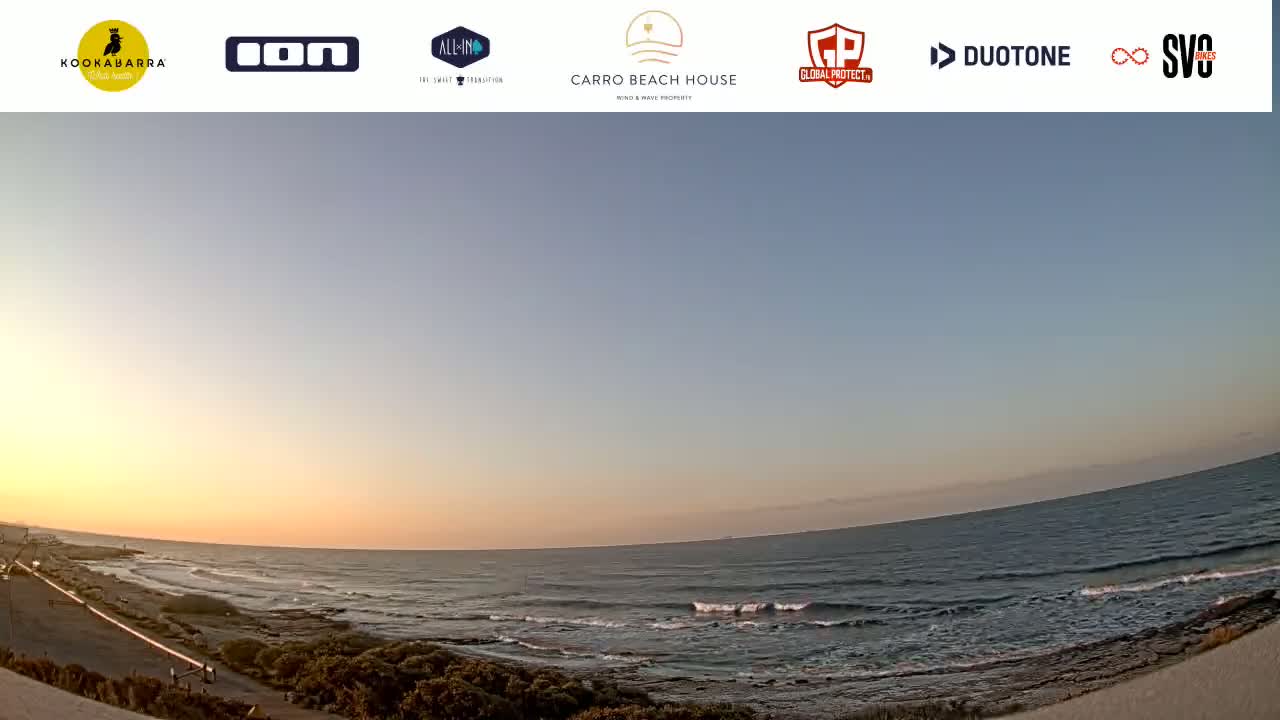 A sunset over a calm ocean with small waves breaking on a rocky shore.