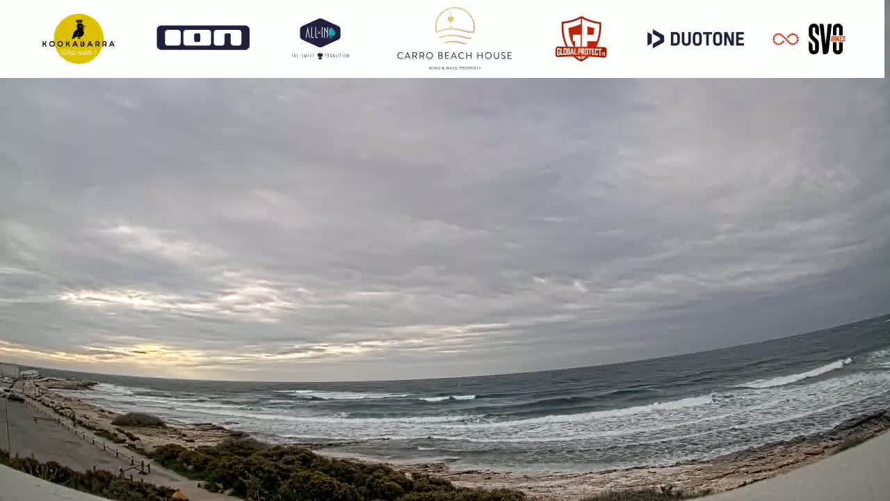 A wide shot of an ocean beach under a mostly cloudy sky, showing small waves breaking on the shore.
