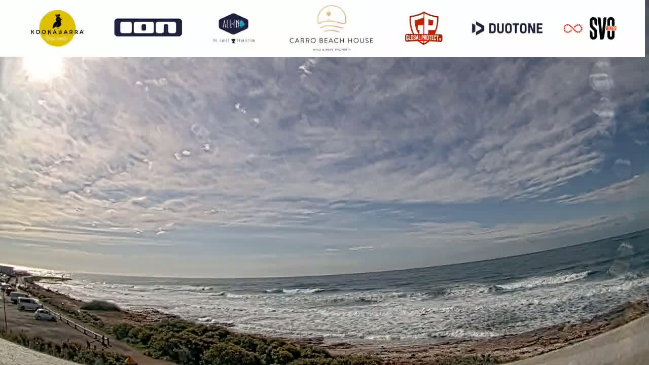 A partly cloudy day shows a view of a rocky coastline and ocean with small waves.