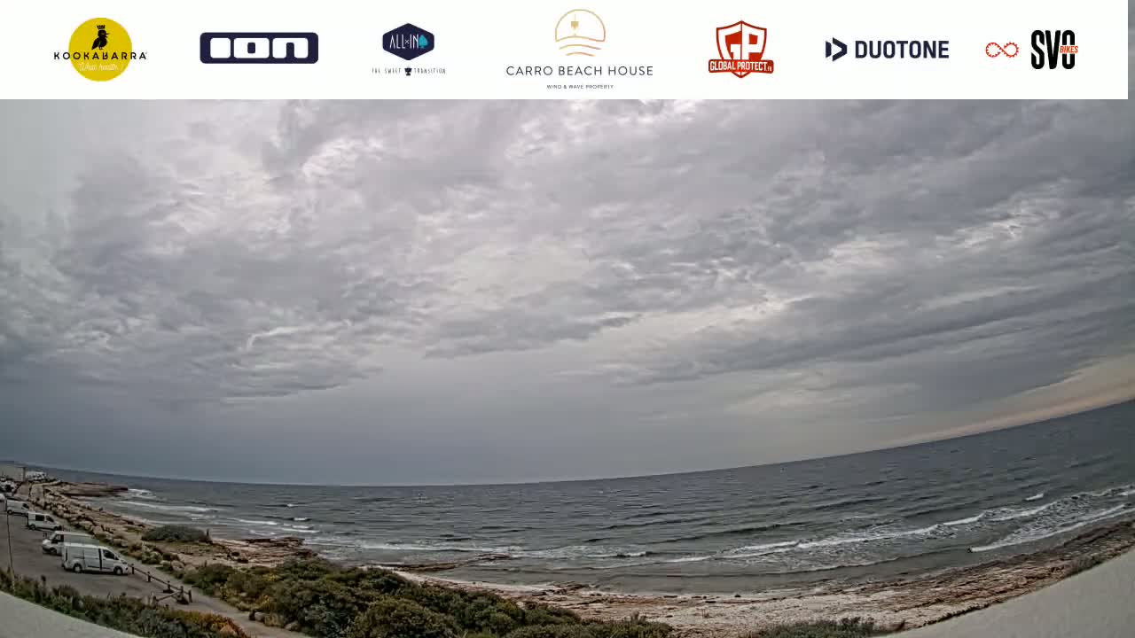 A mostly cloudy sky overlooks a rocky shoreline and a calm ocean with small waves.