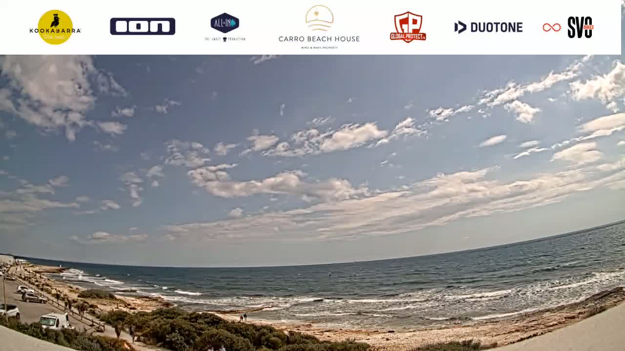 A partly cloudy day overlooks a sandy beach and ocean with small waves.