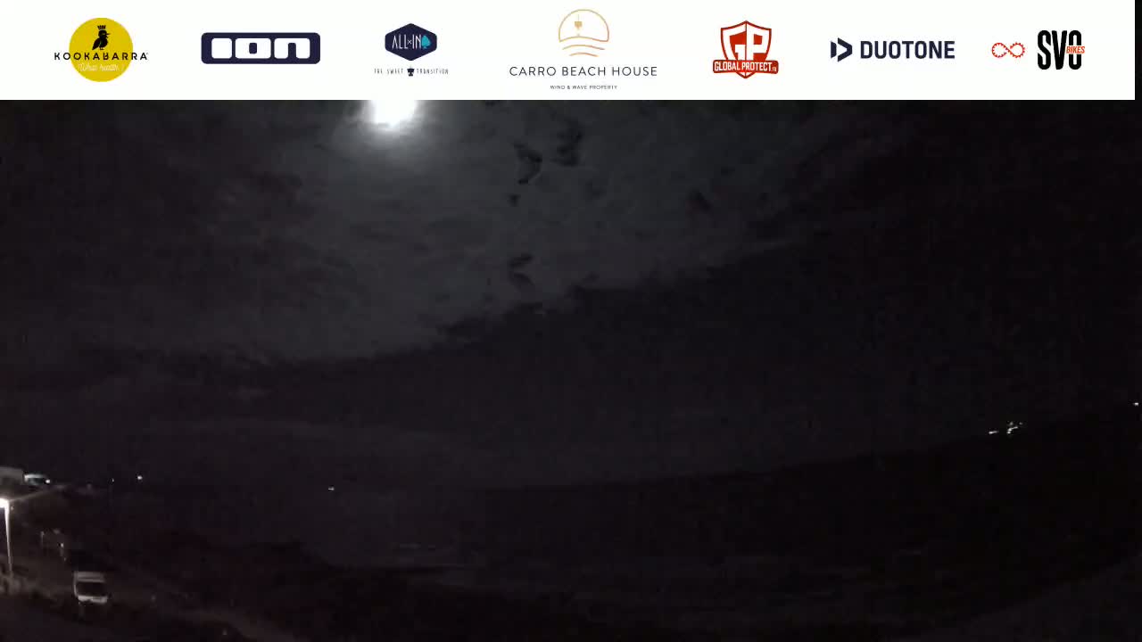 A nighttime view of a dark ocean under a mostly cloudy sky illuminated by a bright moon.