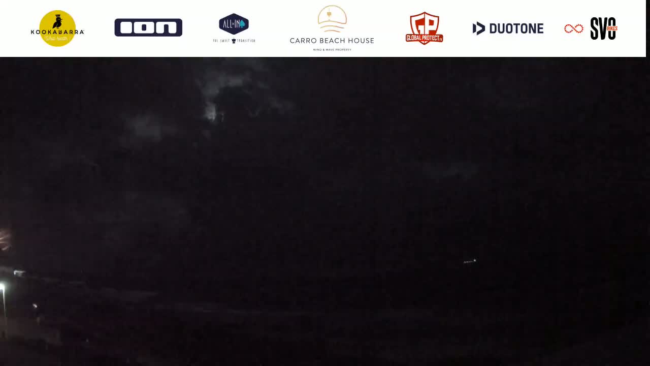 A dark, nighttime coastal scene with a cloudy sky showing faint lightning.