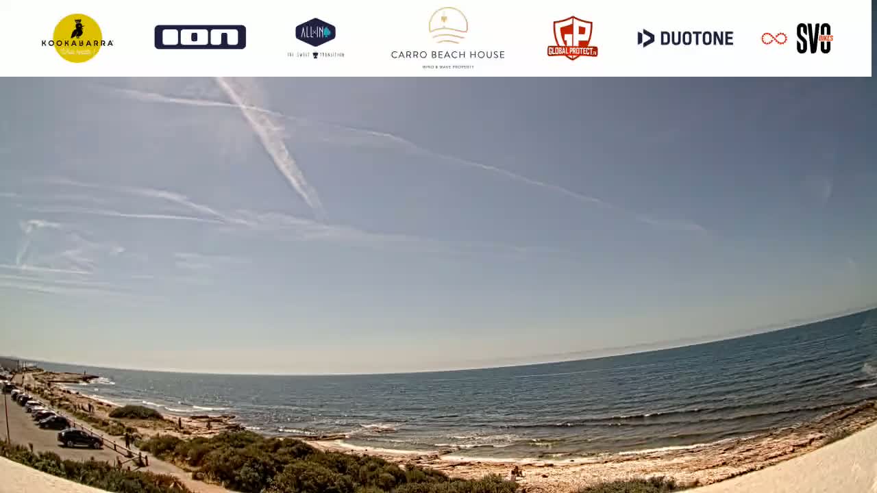 A mostly sunny day at a rocky beach with a calm sea and a few people visible.