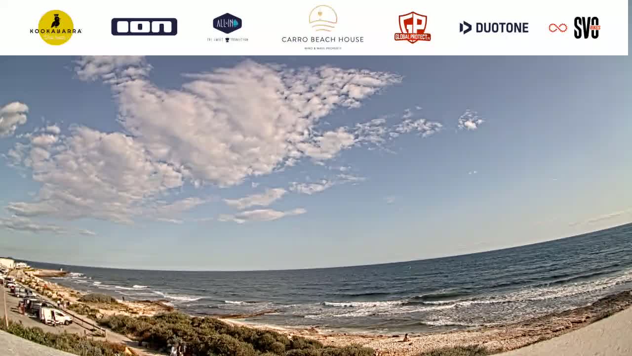 A mostly sunny day with scattered clouds over a beach with calm ocean waves.