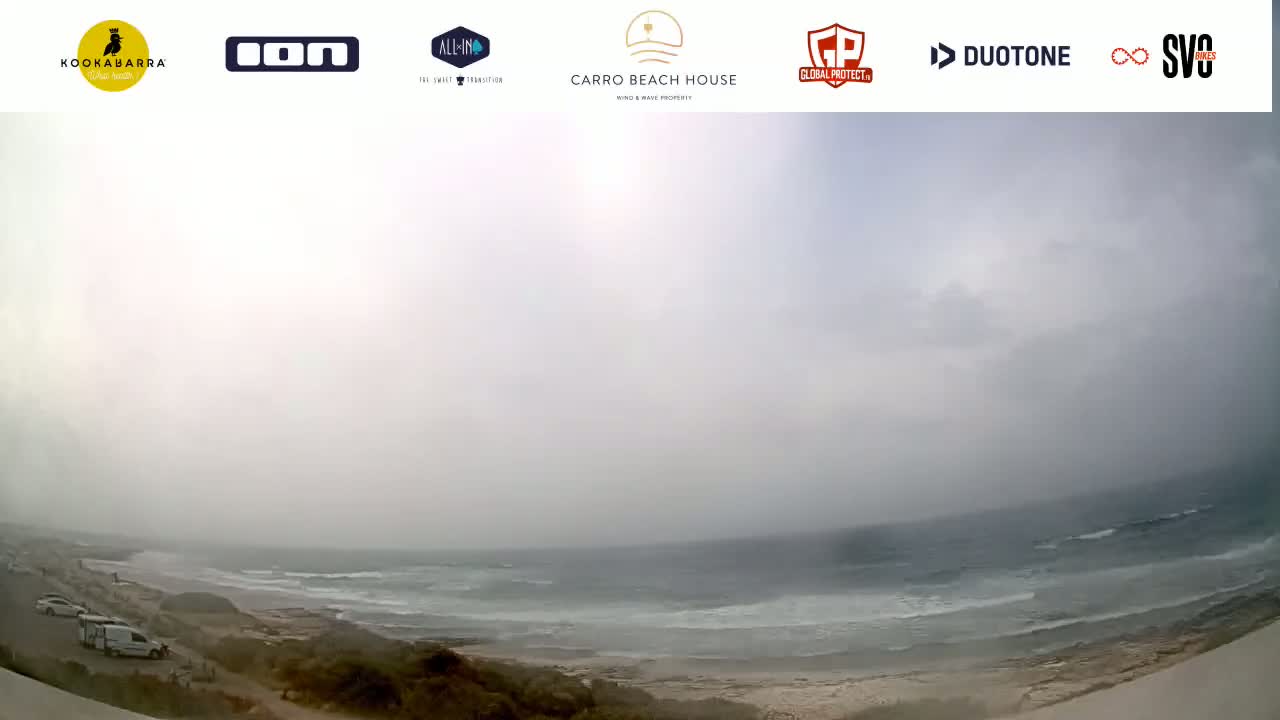 A hazy, overcast day shows a wide view of a beach and ocean with several vehicles parked near the shore.