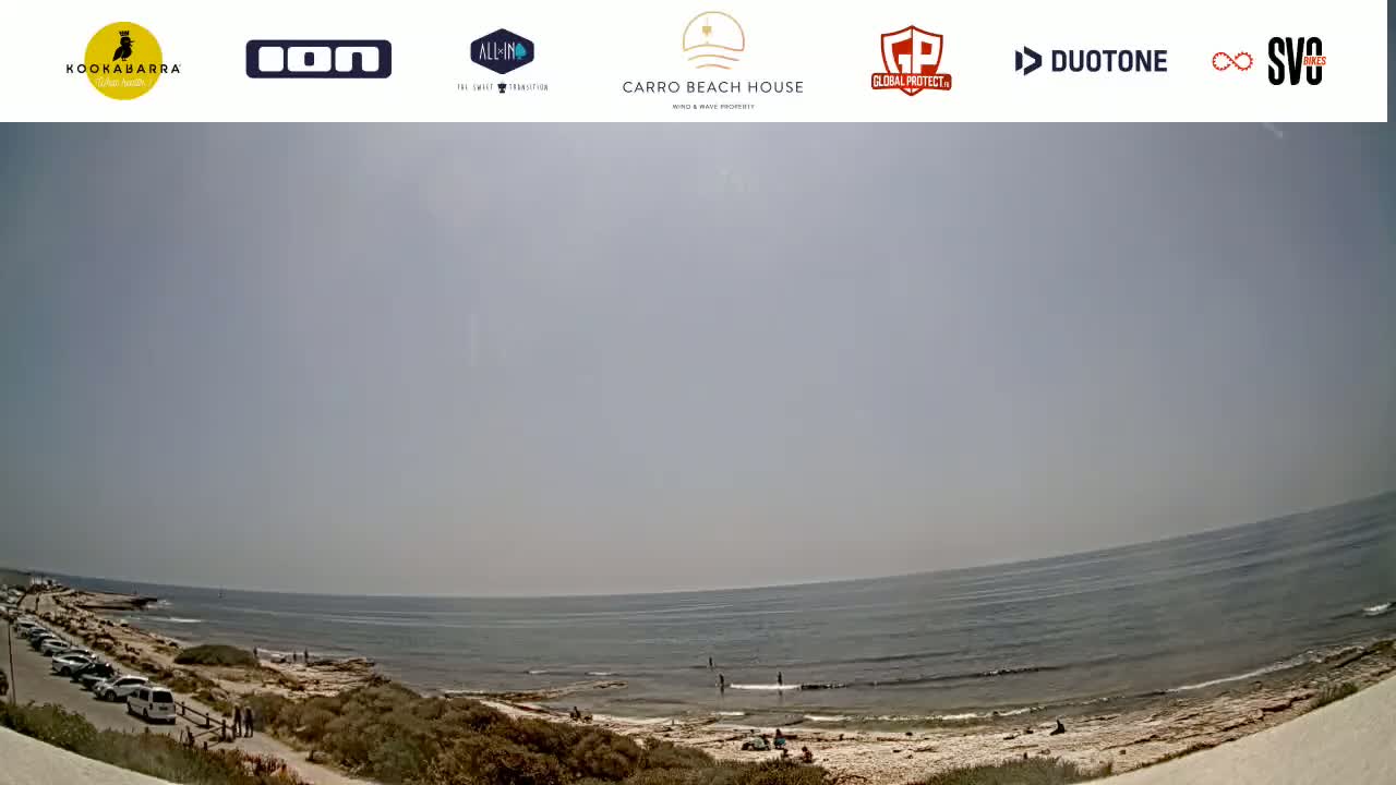 A mostly sunny day at a beach with a calm ocean, a rocky shore, and a few people visible in the distance.