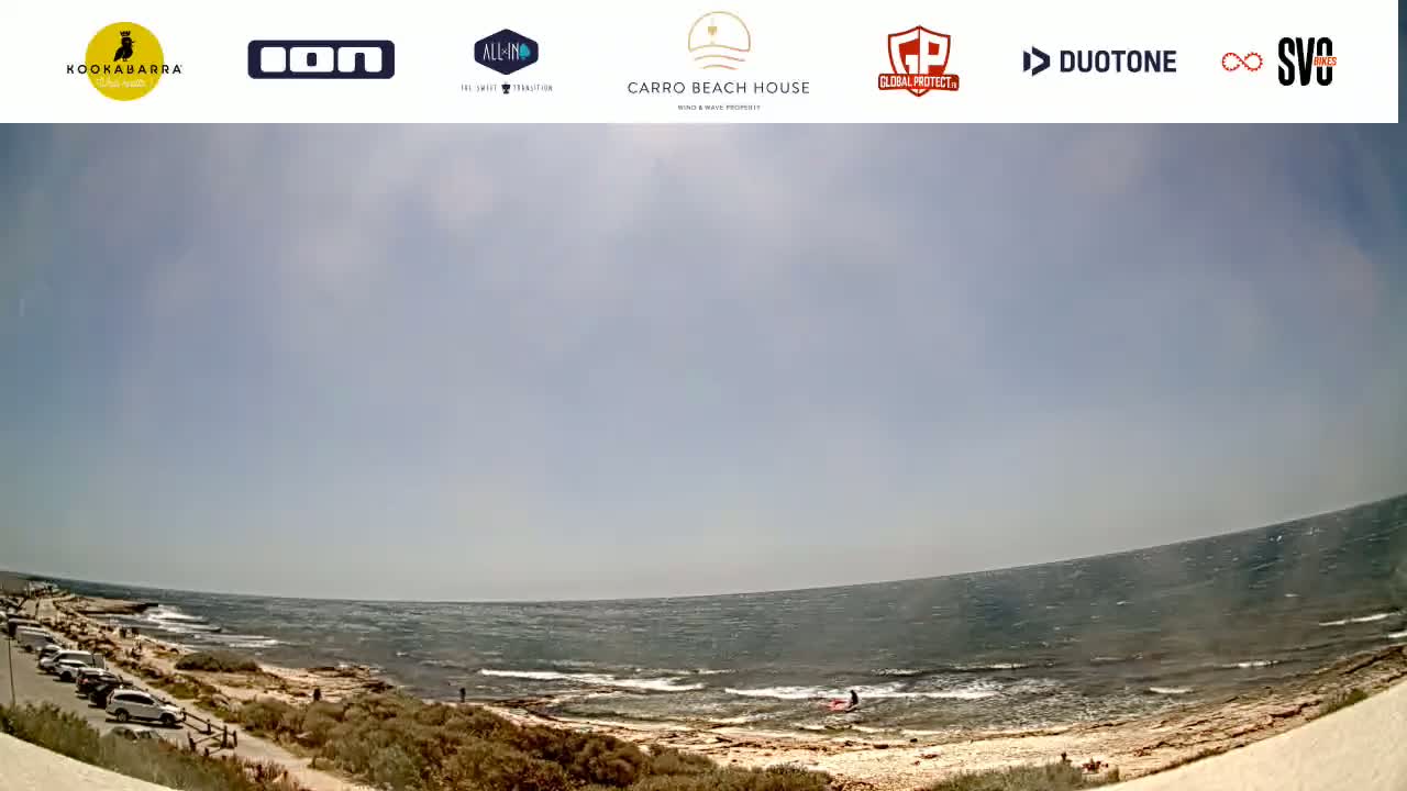 A partly cloudy day at a rocky beach with a person in the water and cars parked nearby.