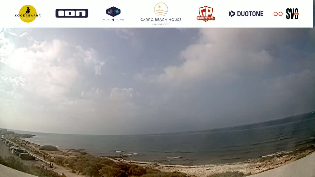 A partly cloudy day overlooks a calm ocean with a sandy beach and a coastal road.