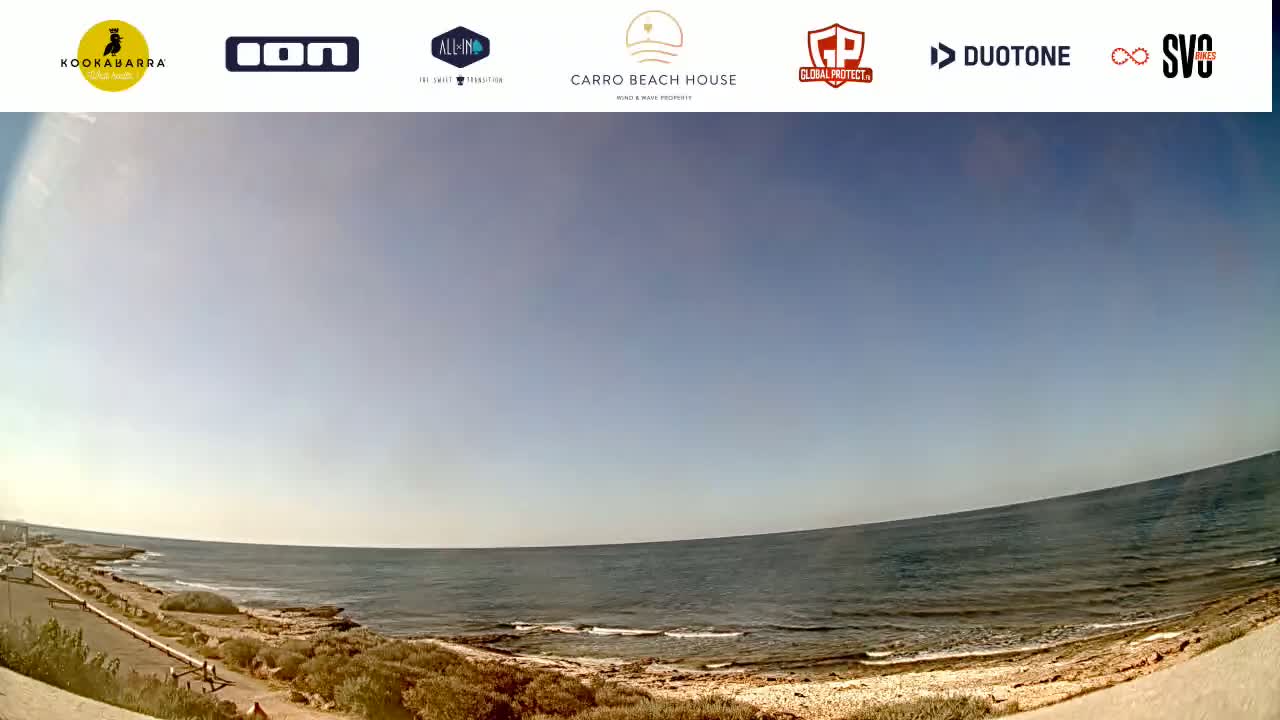 A calm ocean meets a sandy shore under a clear blue sky.