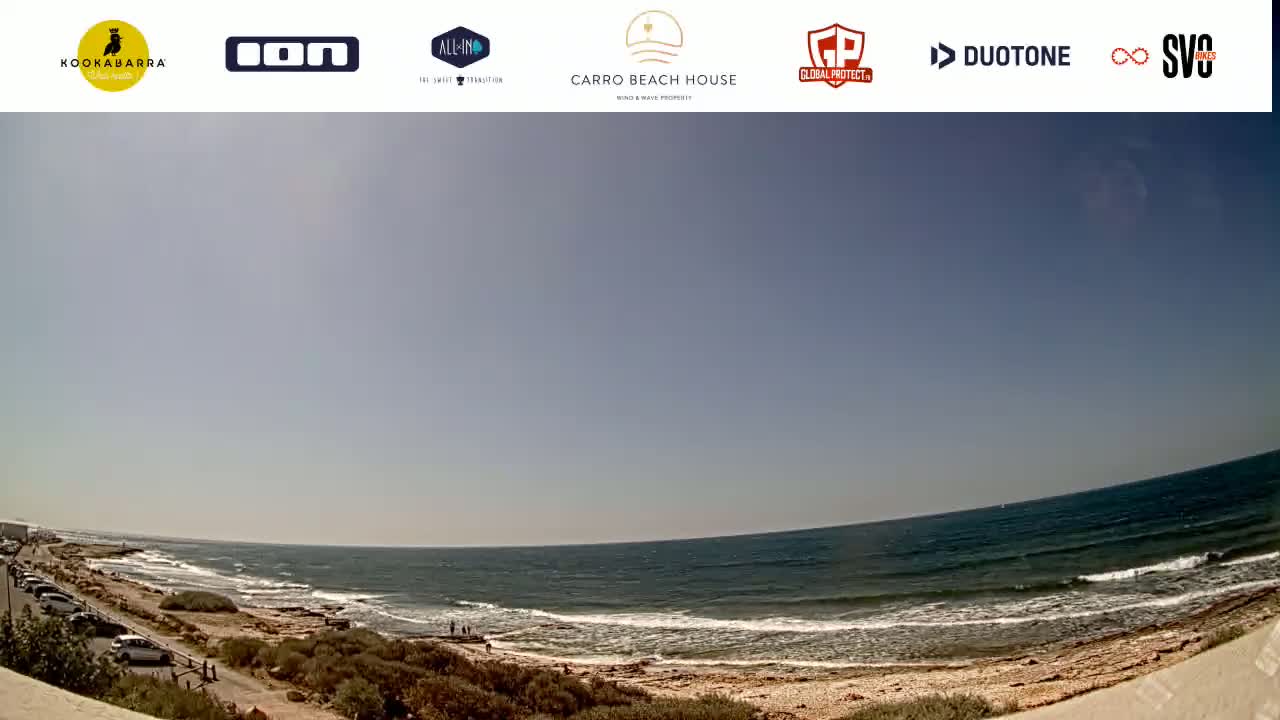 A sunny day at a beach with a calm ocean and a few people visible in the distance.