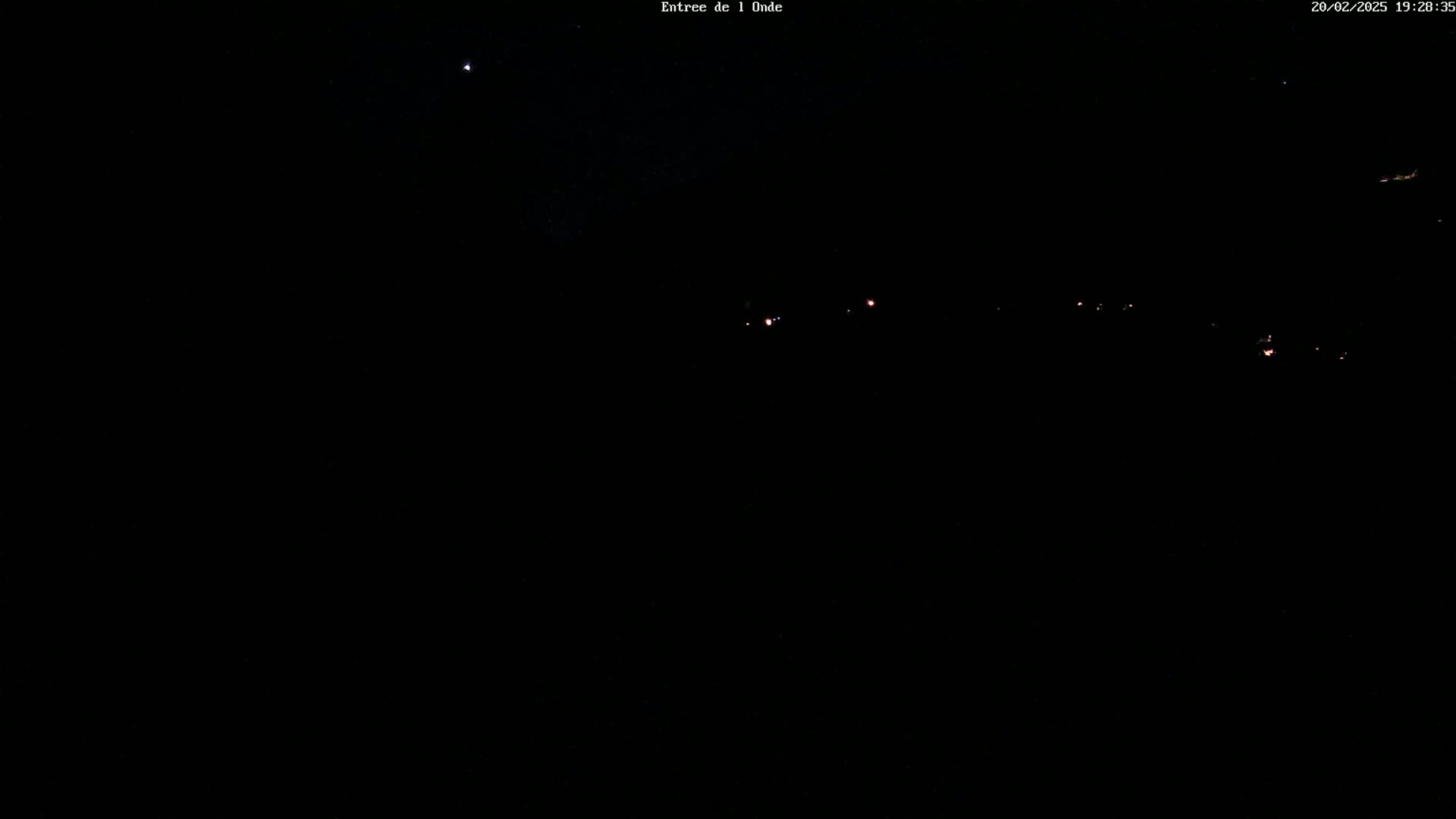 A nighttime view of a dark landscape with a few faint lights visible in the distance and a single bright star in the sky.