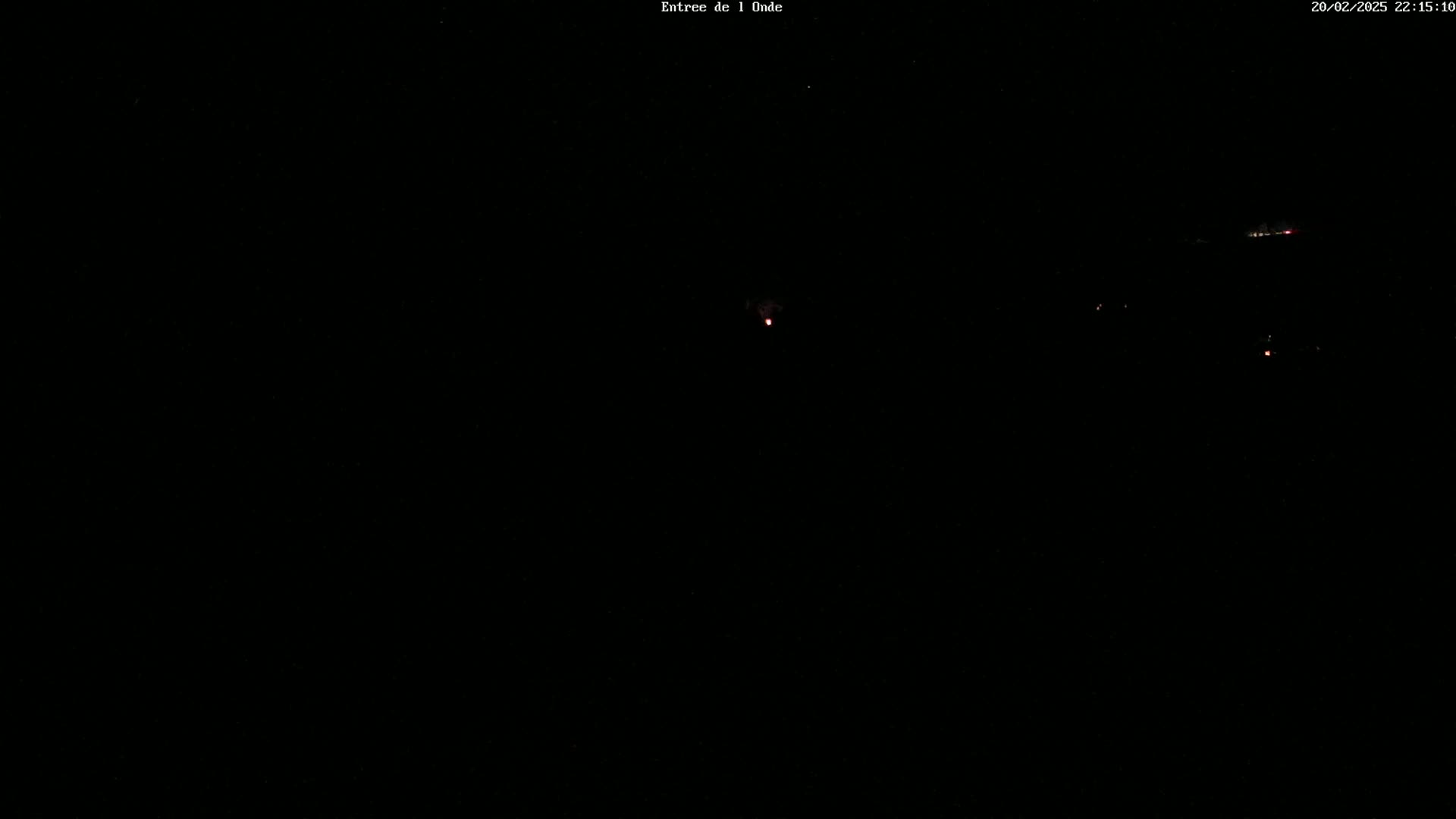 A dark nighttime scene shows a few faint lights in the distance under a clear, starry sky.