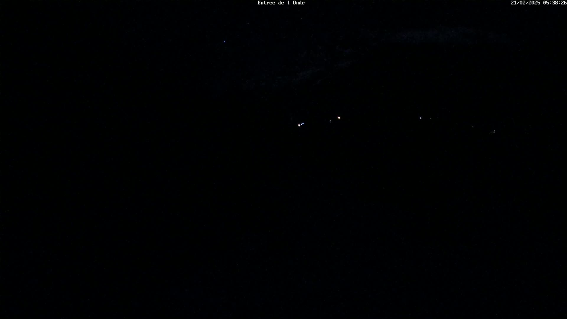 A dark, nighttime scene shows a few faint lights in the distance under a mostly clear sky.