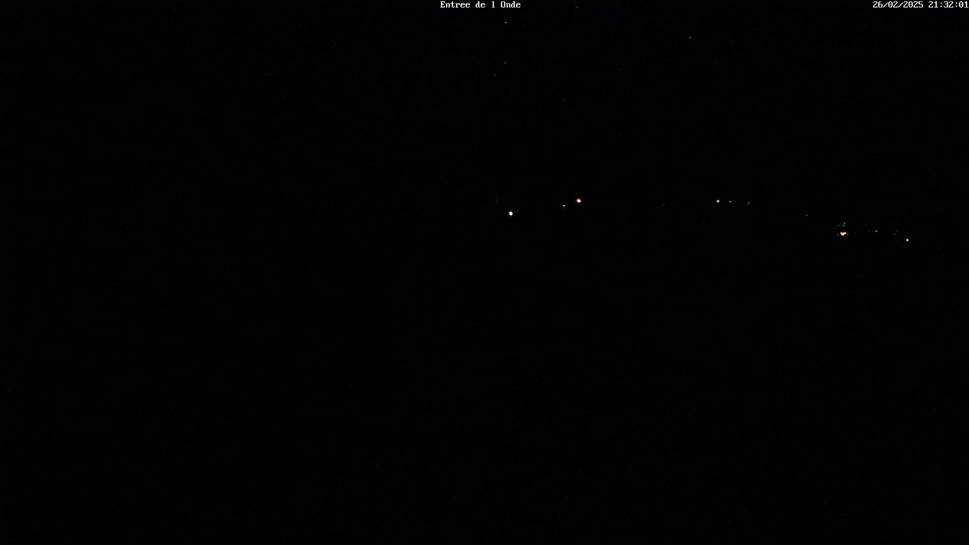 A dark nighttime scene shows a distant line of faint lights on a dark horizon under a clear, starry sky.