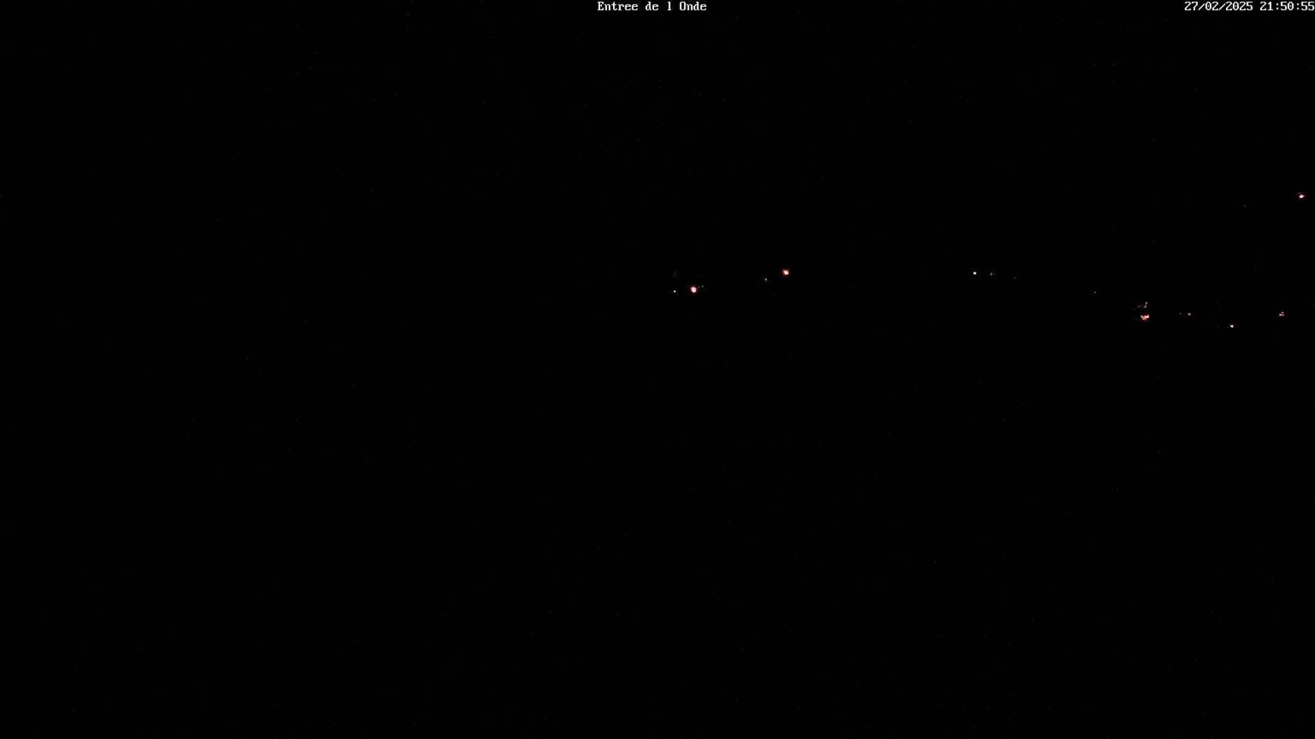A nighttime, dark scene with a few faint red lights visible in the distance.