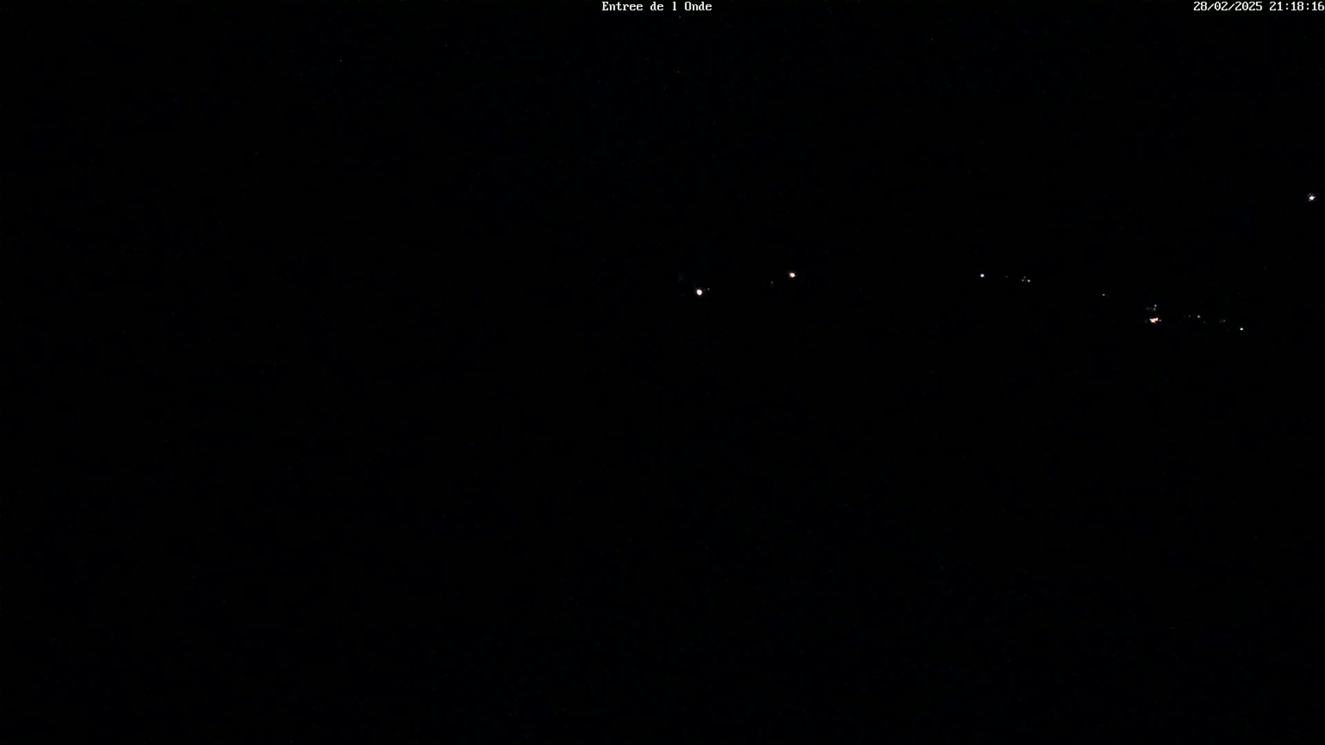 A dark nighttime scene shows a few distant lights on a dark horizon under a clear, starlit sky.