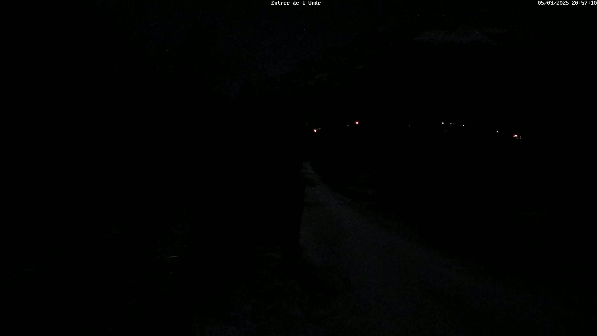 A dark, nighttime scene shows a road with faint red lights in the distance under a clear sky.