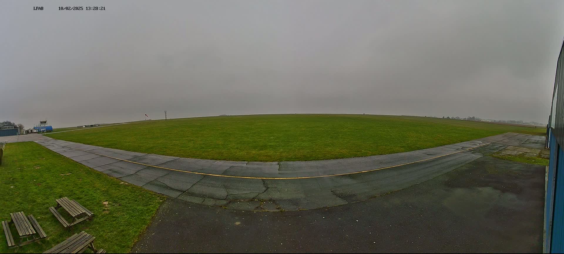 A grassy airfield with a paved taxiway is visible under an overcast sky.