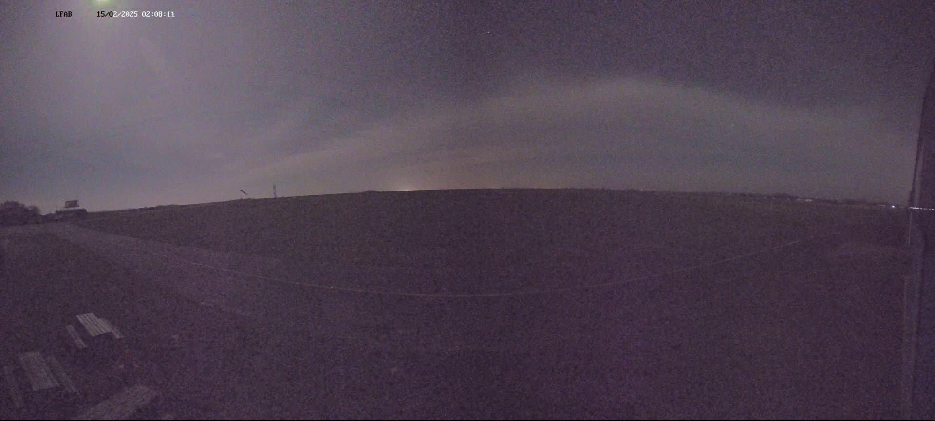 A dark, flat field is visible under a night sky with a faint, light-colored band near the horizon.