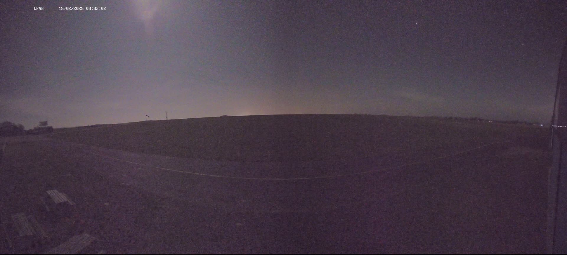 A dark, flat field is visible under a night sky with a faint moon or light source.
