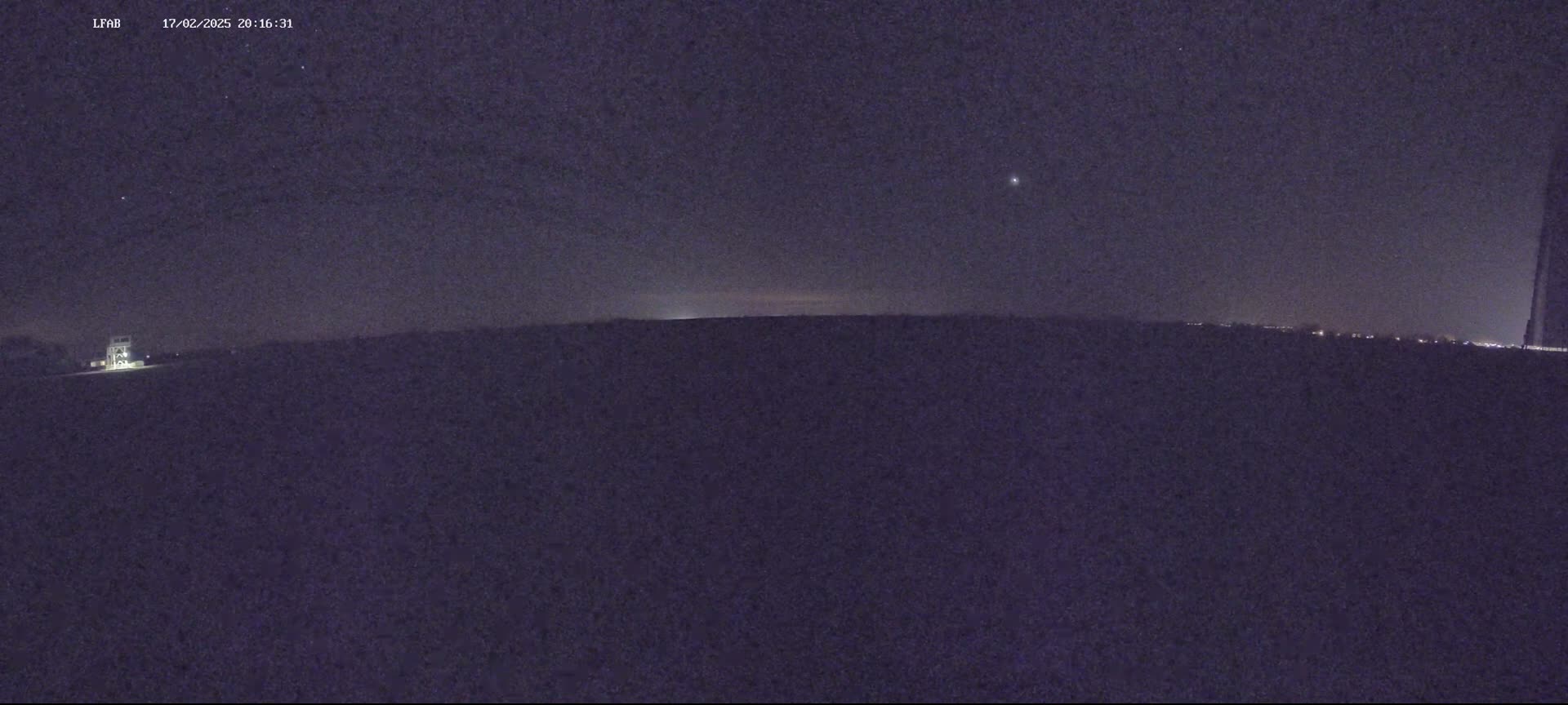 A nighttime, low-light view of a dark landscape under a mostly clear sky with a few visible stars.