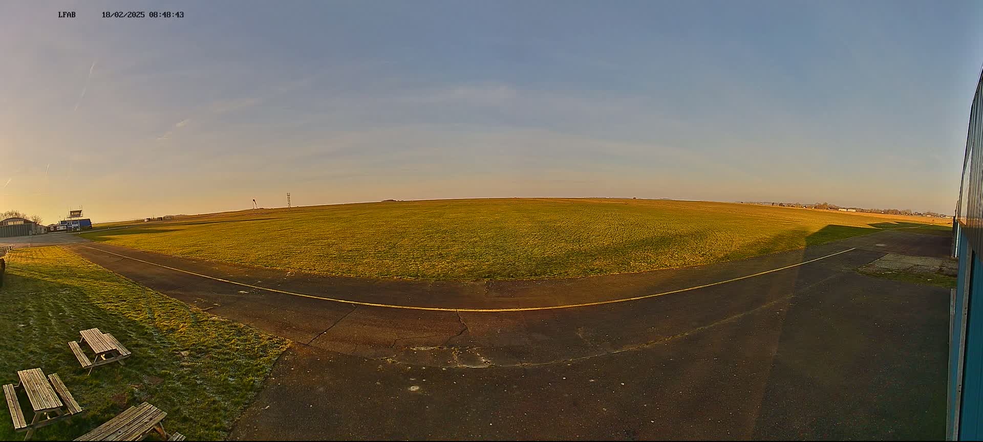 A wide, grassy airfield with a paved taxiway is visible under a clear, twilight sky.
