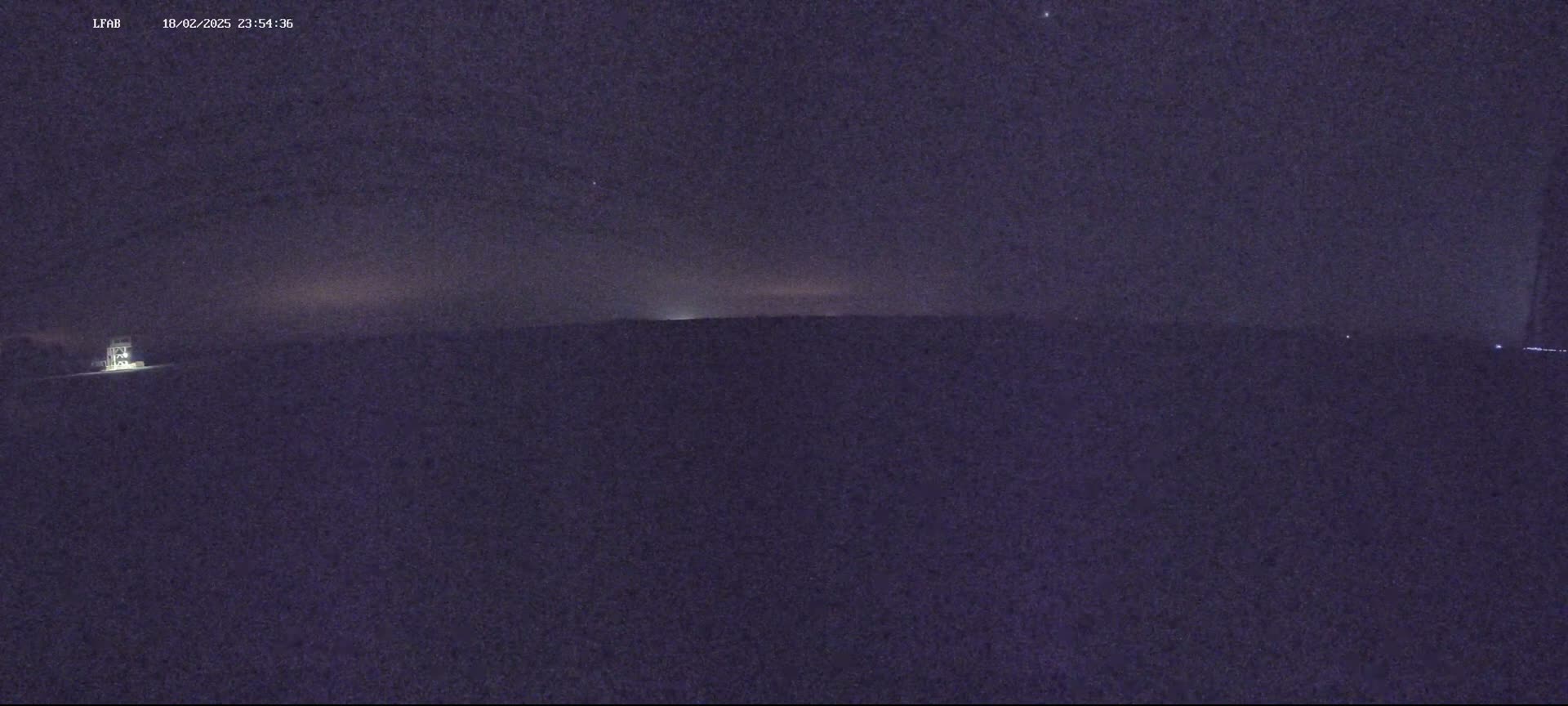 A nighttime, low-light view of a flat, dark landscape under a mostly clear, dark sky.