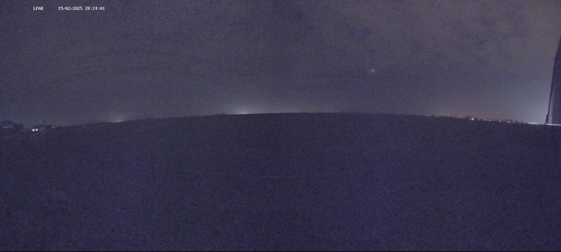 A dark, flat landscape is visible under a mostly clear night sky with a few faint lights in the distance.