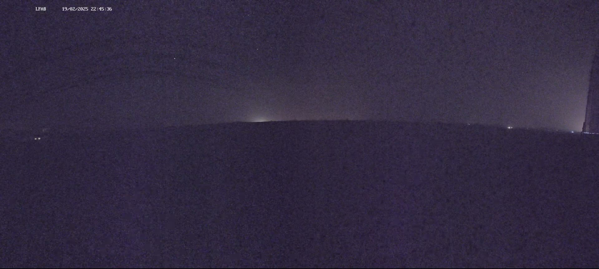 A dark, nighttime landscape is visible, showing a flat horizon under a mostly clear, starry sky.
