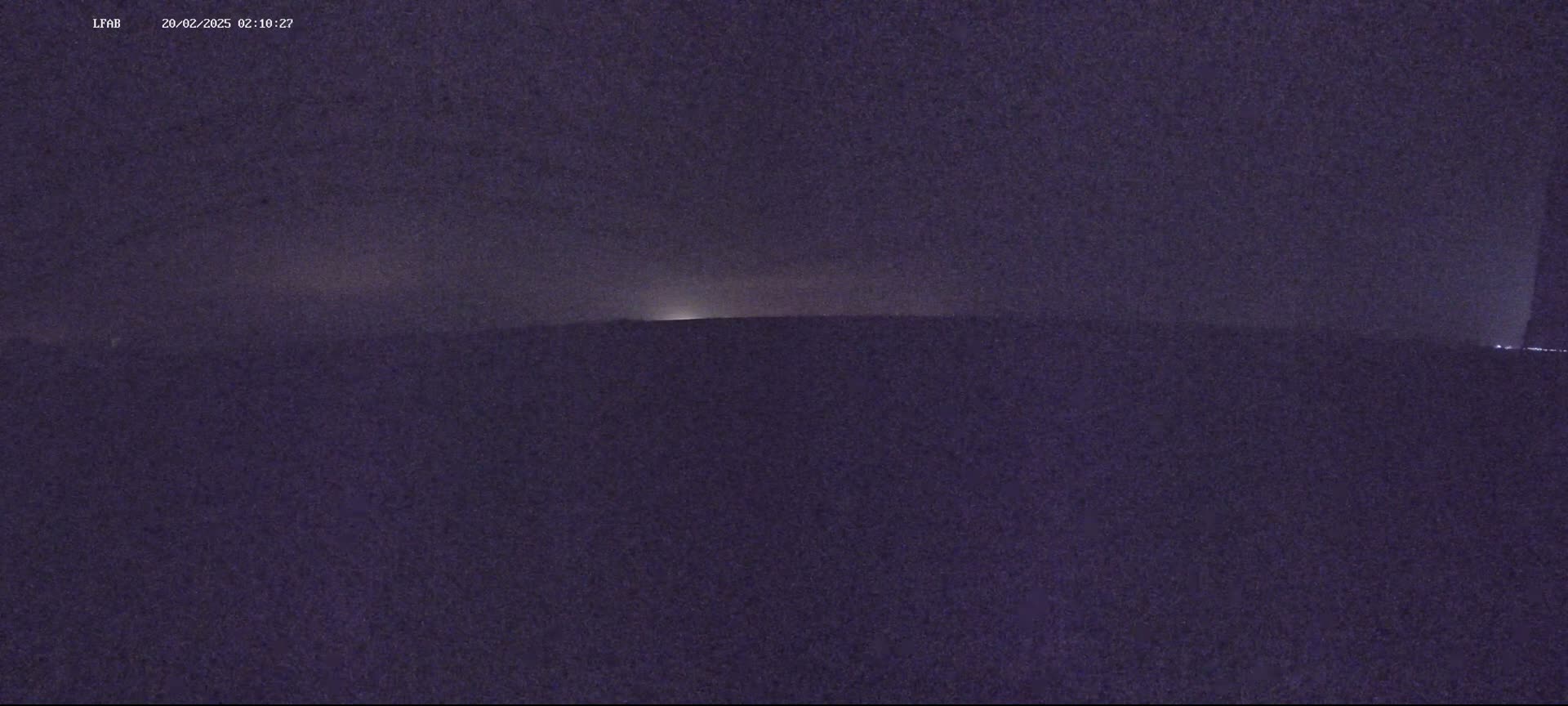 A dark, nighttime landscape is visible under a mostly cloudy sky with a faint glow on the horizon.