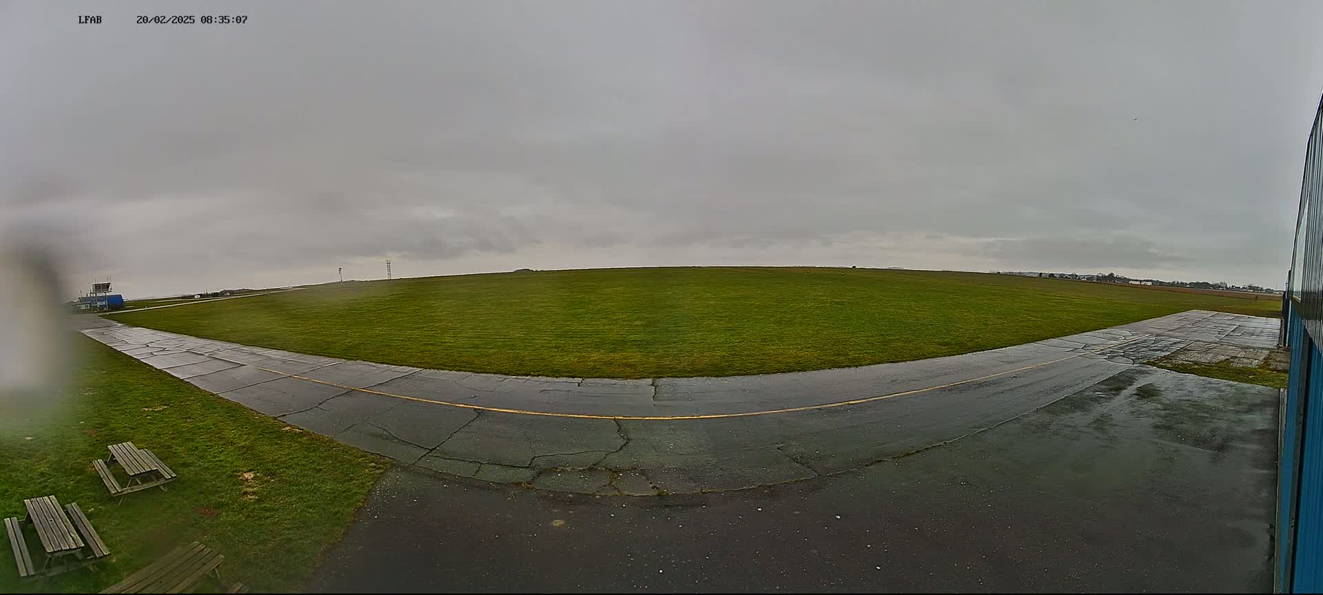 A wet, grassy airfield is viewed from a low angle on an overcast day.