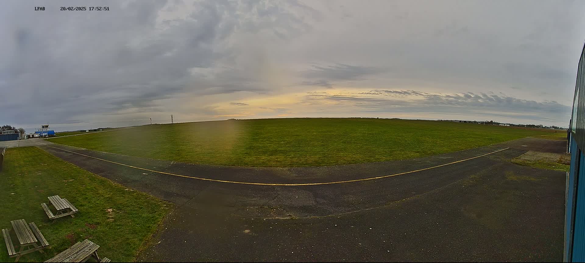 A grassy airfield with a paved taxiway is visible under an overcast sky with a hint of sunset.