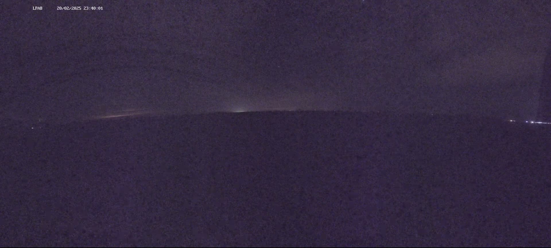A dark, nighttime landscape is visible, with a faint, horizontal light source on the horizon.