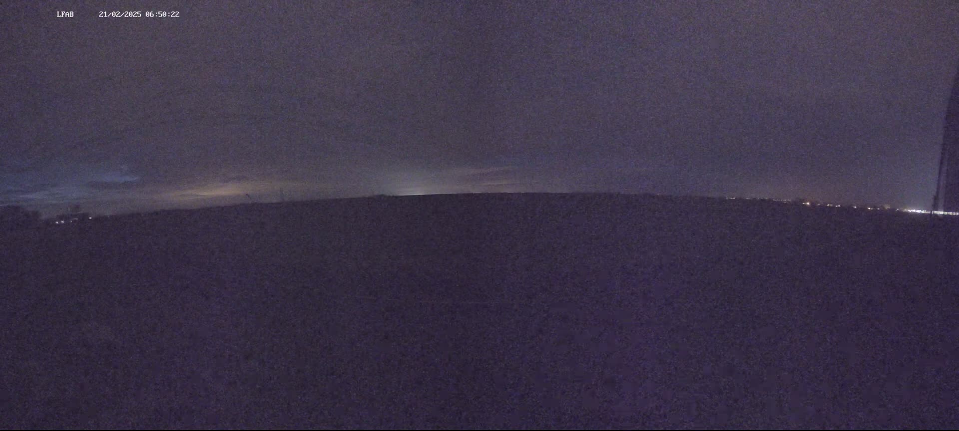 A dark, flat landscape is visible under a mostly cloudy, twilight sky.