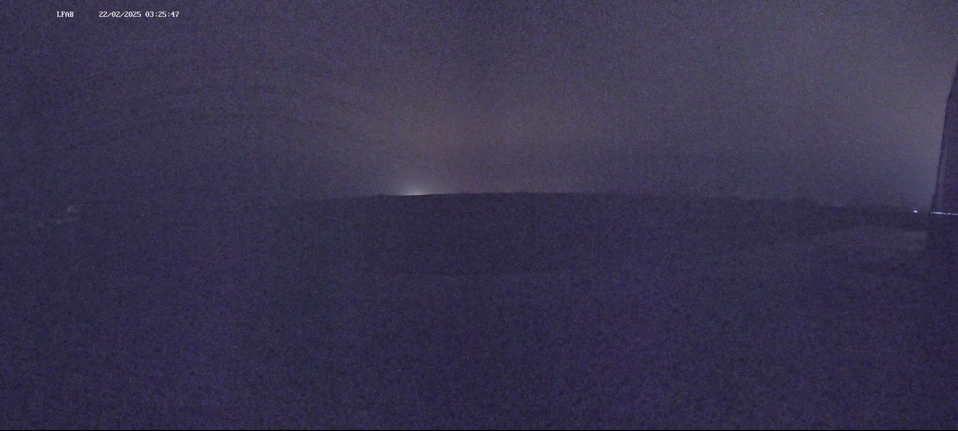 A dark, possibly nighttime, outdoor scene shows a flat horizon line under a dusky sky with a faint light source in the distance.
