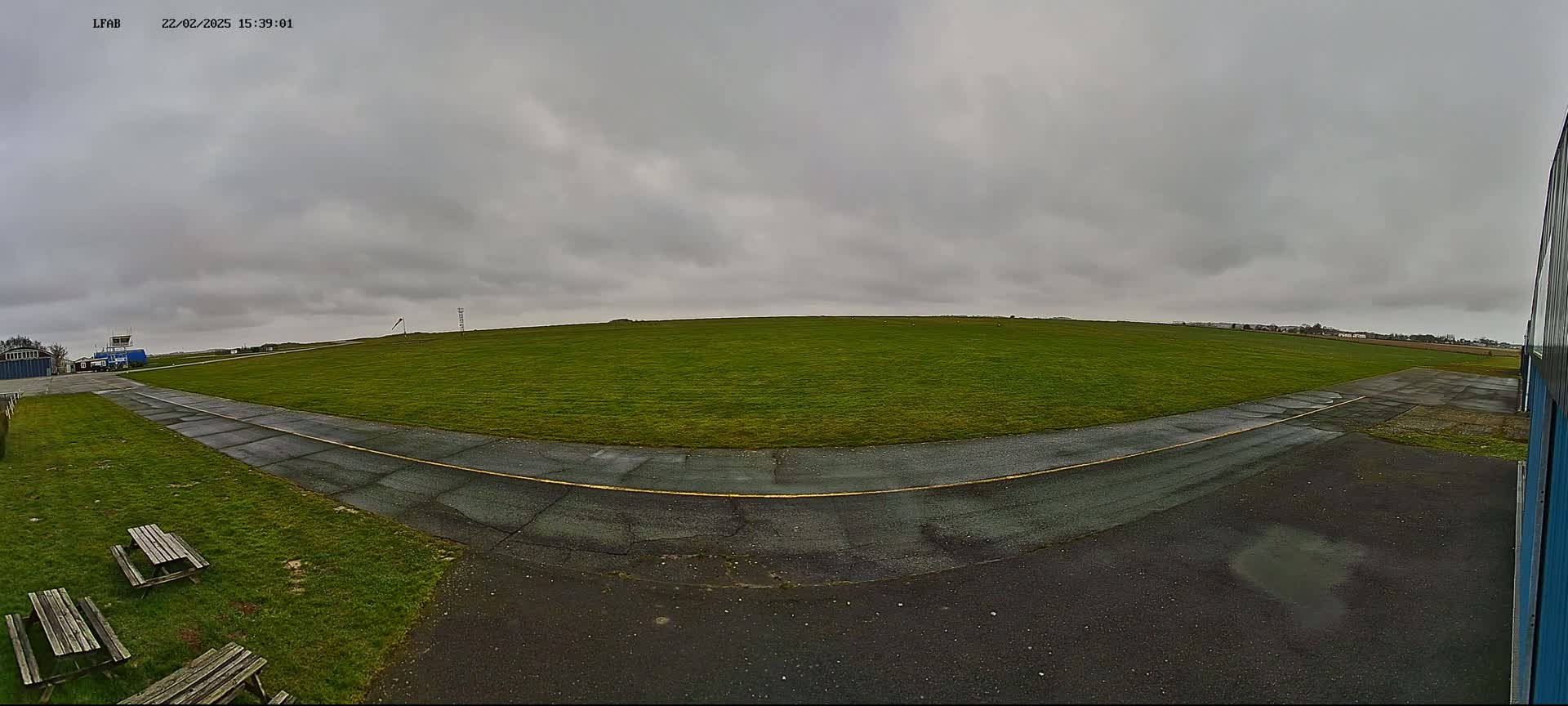 A wide, grassy airfield with a paved taxiway curves to the left, under an overcast sky.