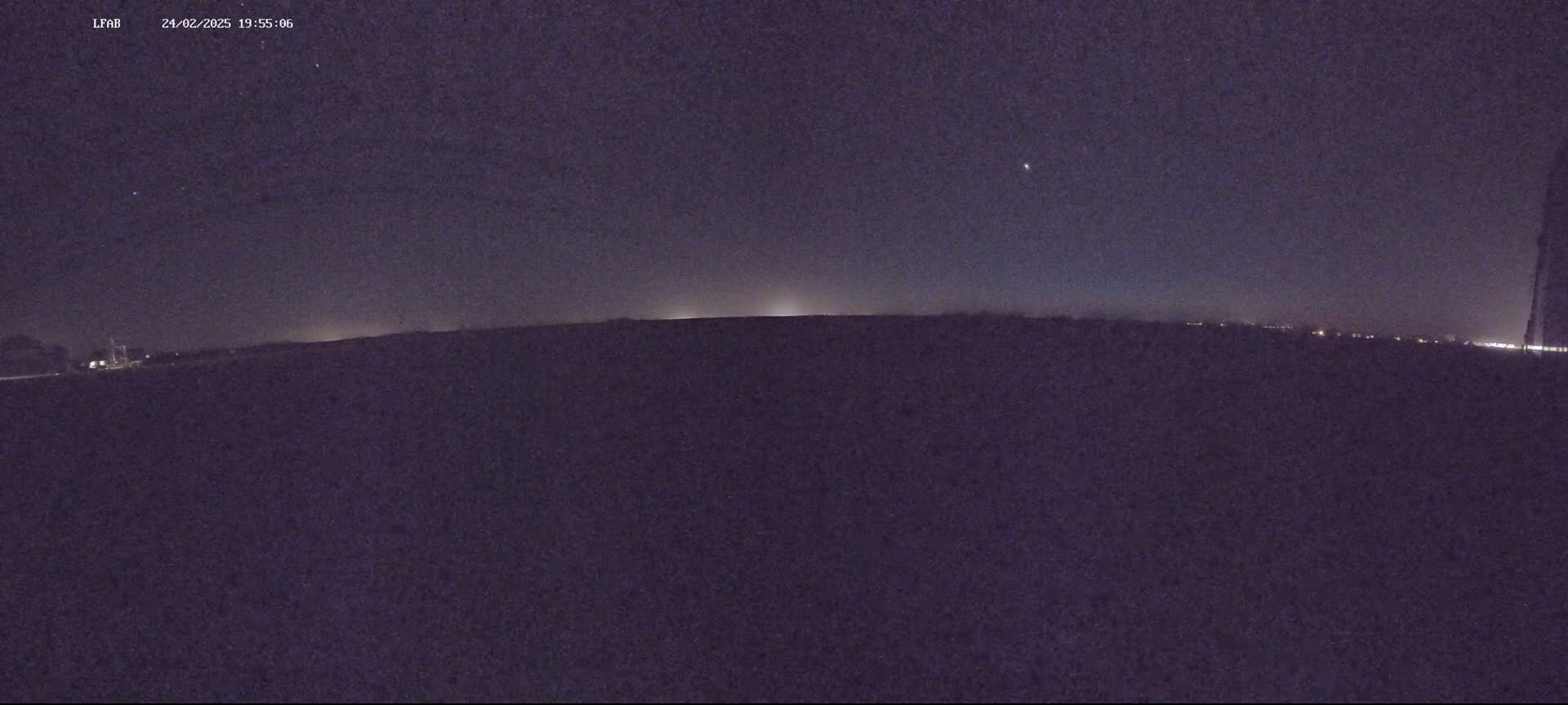 A dark, flat landscape is visible under a mostly clear night sky with a few faint stars.