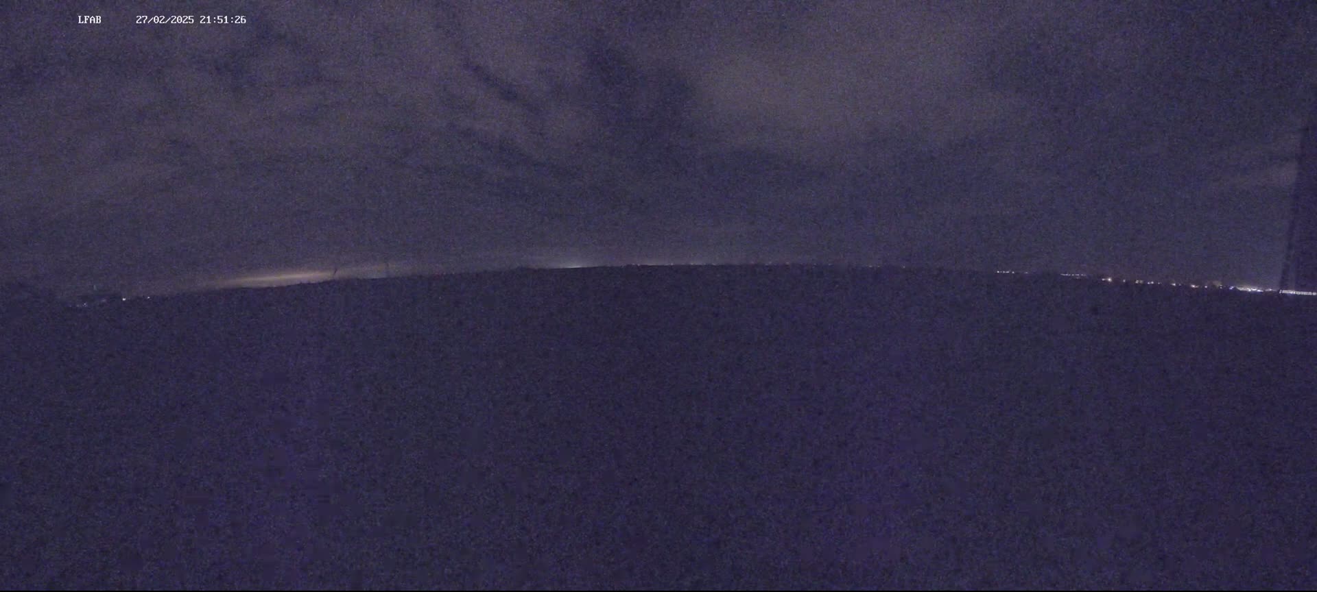 A dark, nighttime landscape is visible under a cloudy sky, with a faint horizon line showing distant lights.