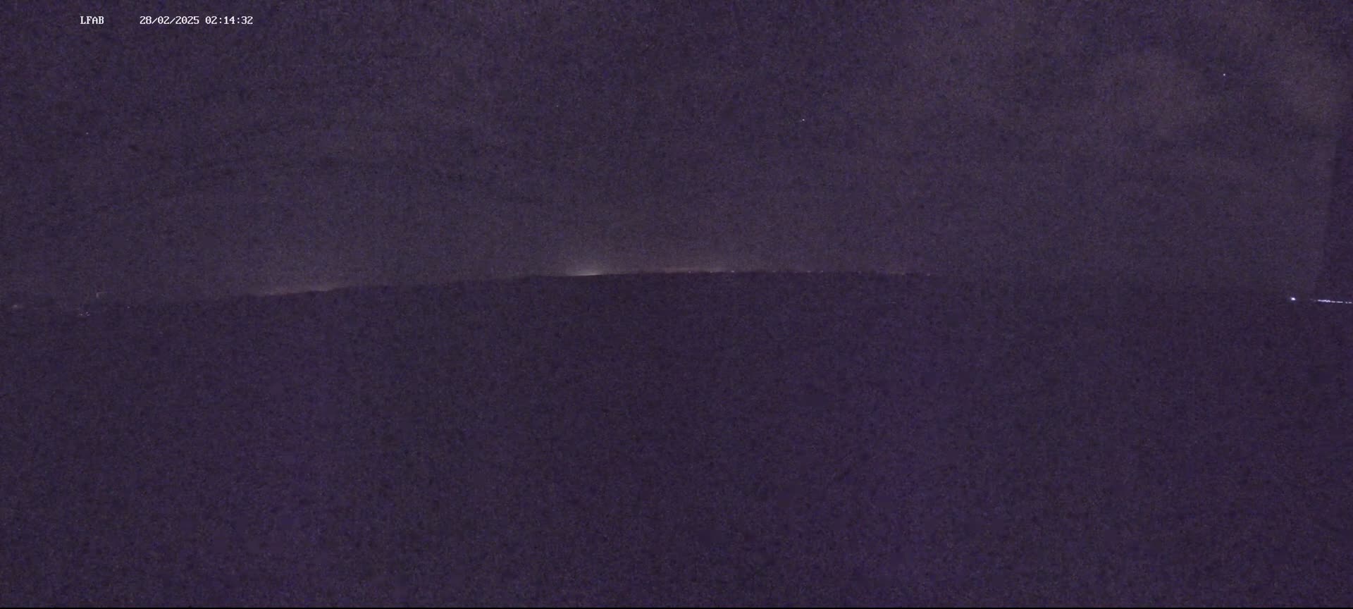A dark, nighttime landscape shows a dimly lit horizon line under a mostly clear sky.
